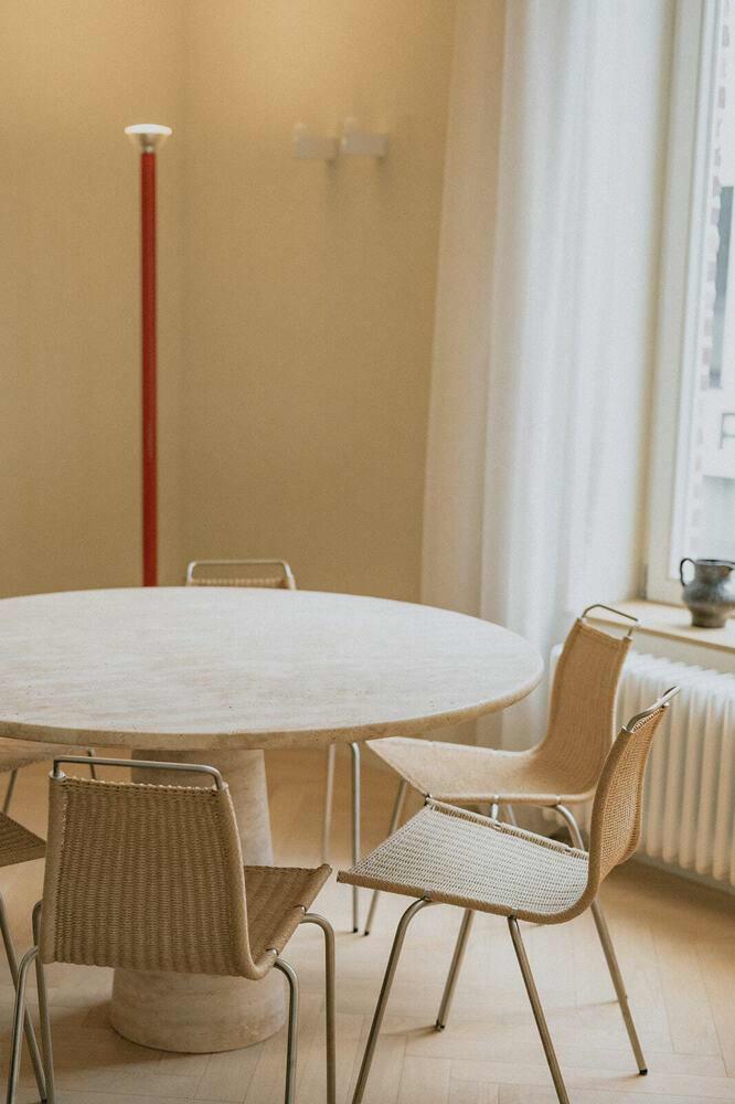 Vintage travertin eettafel met Fritz Hansen stoelen en een opvallende rode Flos lamp in een warm, stijlvol appartement.