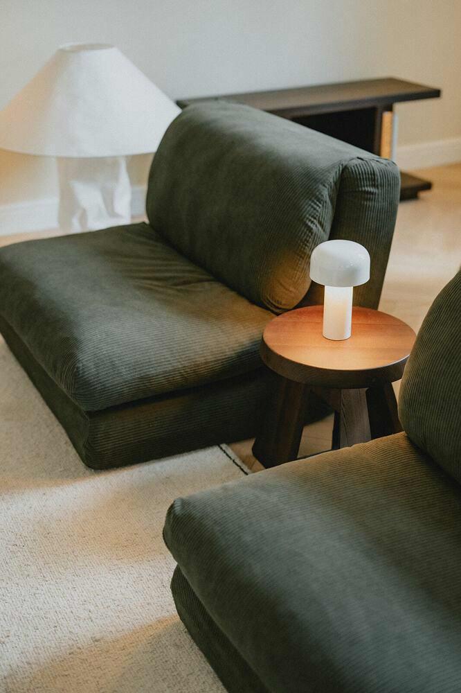 Intieme zithoek met groene eenzitjes, designlamp en zacht tapijt op een klassiek Haussmann parket.